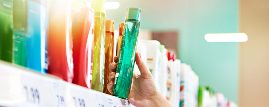 Mano seleccionando un envase de shampoo verde de una góndola.